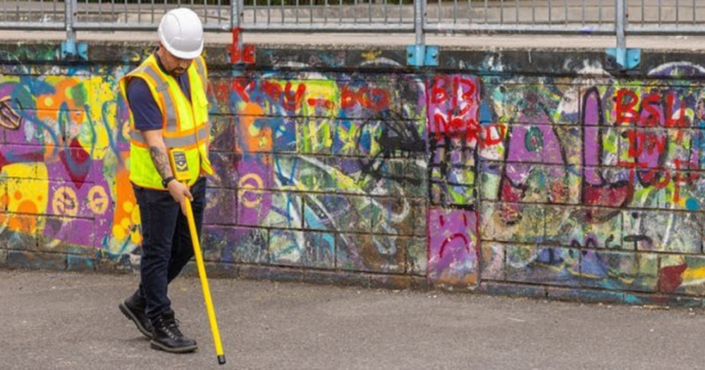 A man in a safety vest using a magnetic locator on a sidewalk.