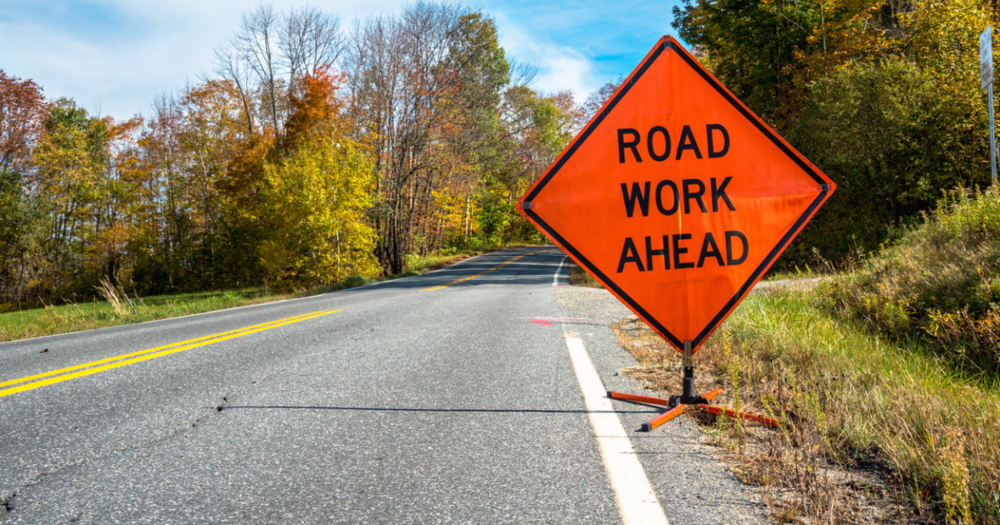 A foldable traffic sign saying road work ahead on the shoulder of a road.