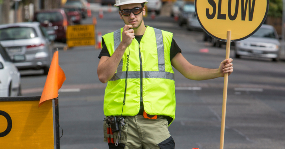 A man holding a slow sign to help control traffic for a road work crew.