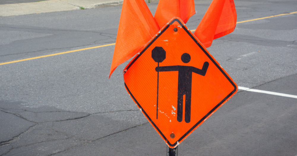 An orange traffic control sign with flags attached.