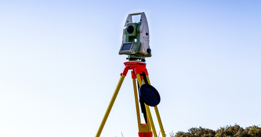 A robotic total station for land surveying against a blue sky.