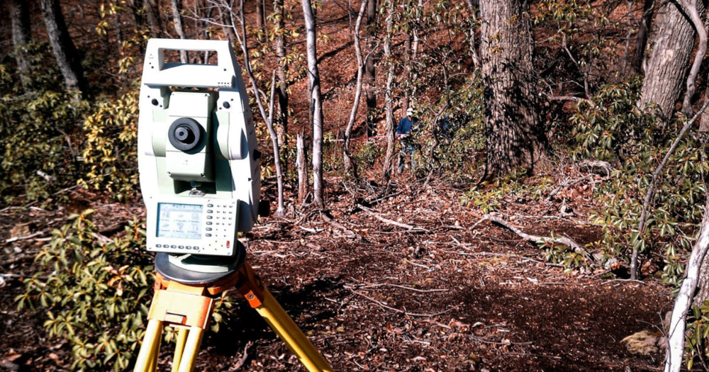 A total station being used in the woods.