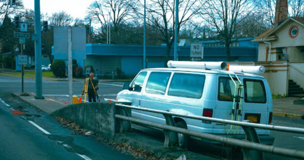 A land surveyor on a street next to his van using a total station. A land surveyor on a street next to his van using a total station.