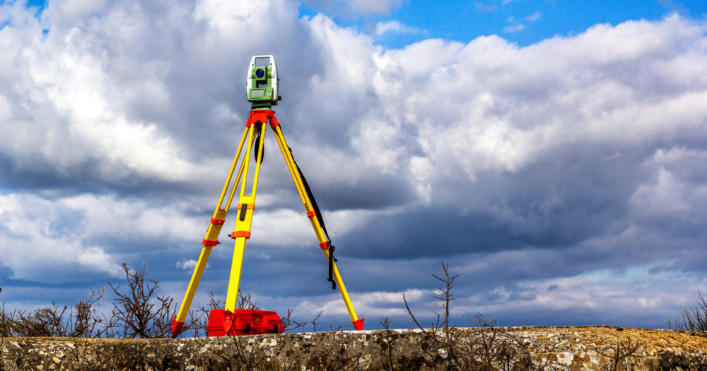 A total station setup in a field against a blue sky.
