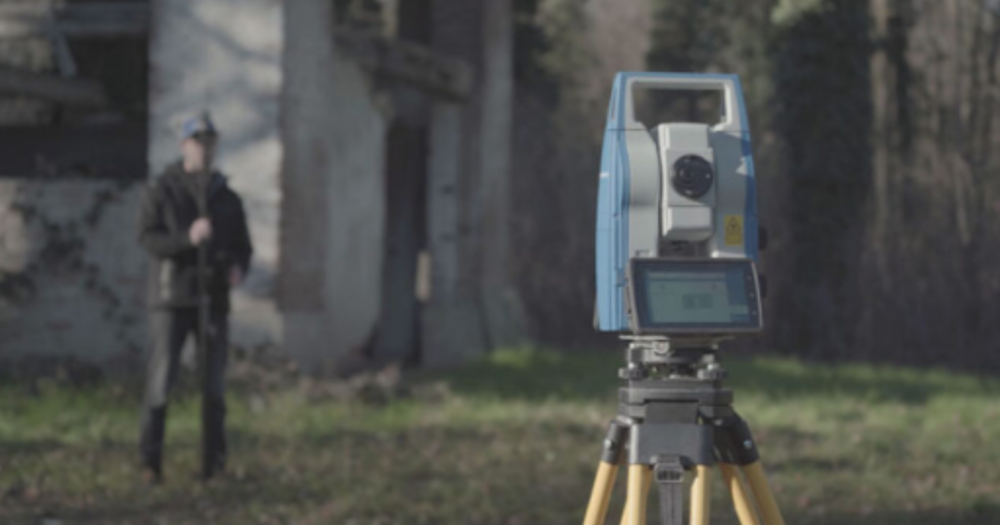 A total station and a surveyor holding a prism near a building. A total station and a surveyor holding a prism near a building.
