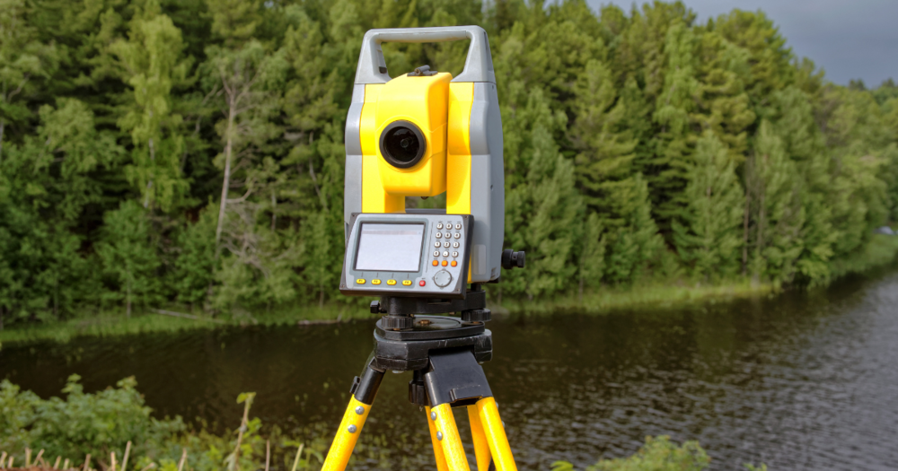 A yellow total station next to a river.