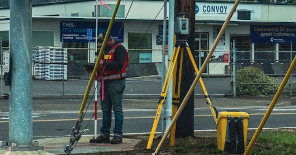 A surveyor at a street corner using a prism to take measurments.